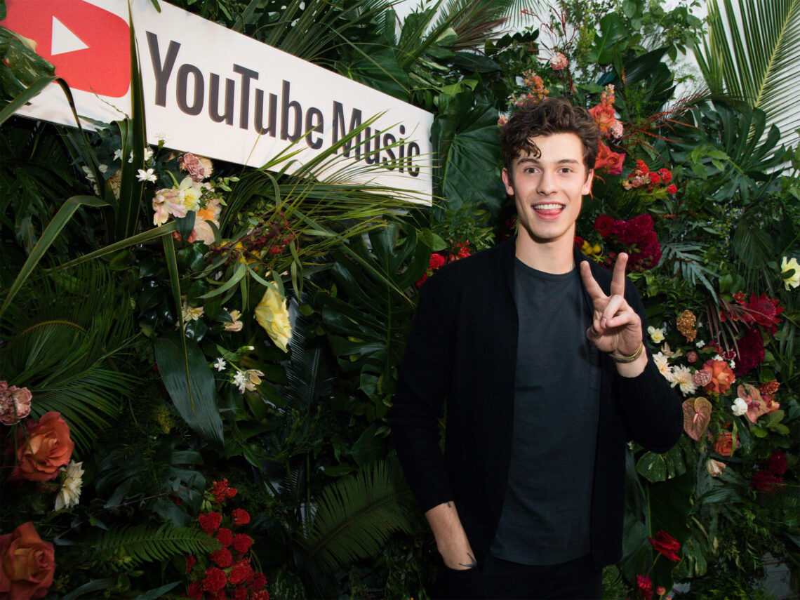 Shawn Mendez at YouTube event with flower wall behind him