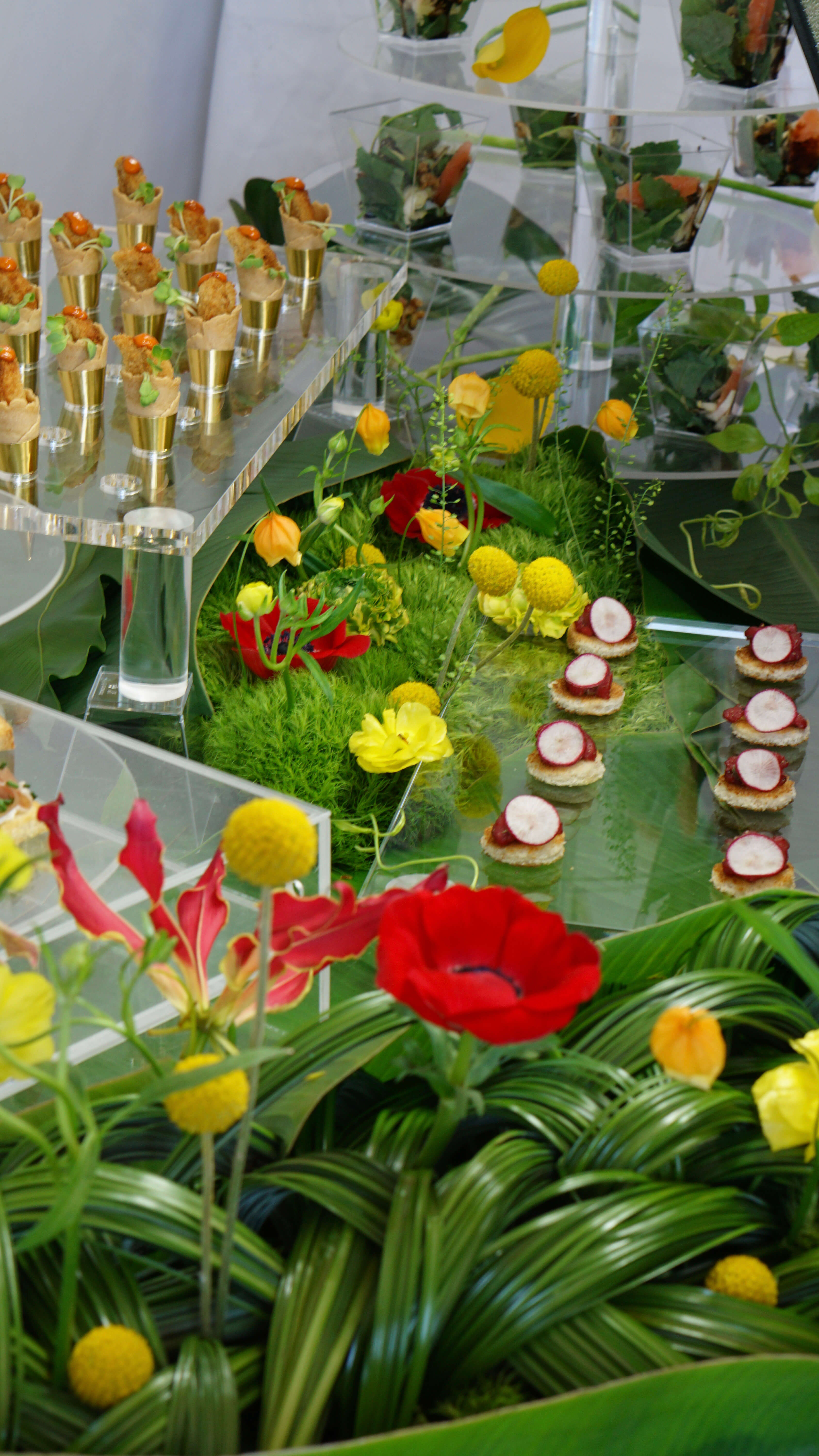 Green food station design incorporating multiple hors d'oeuvres and red and yellow flowers
