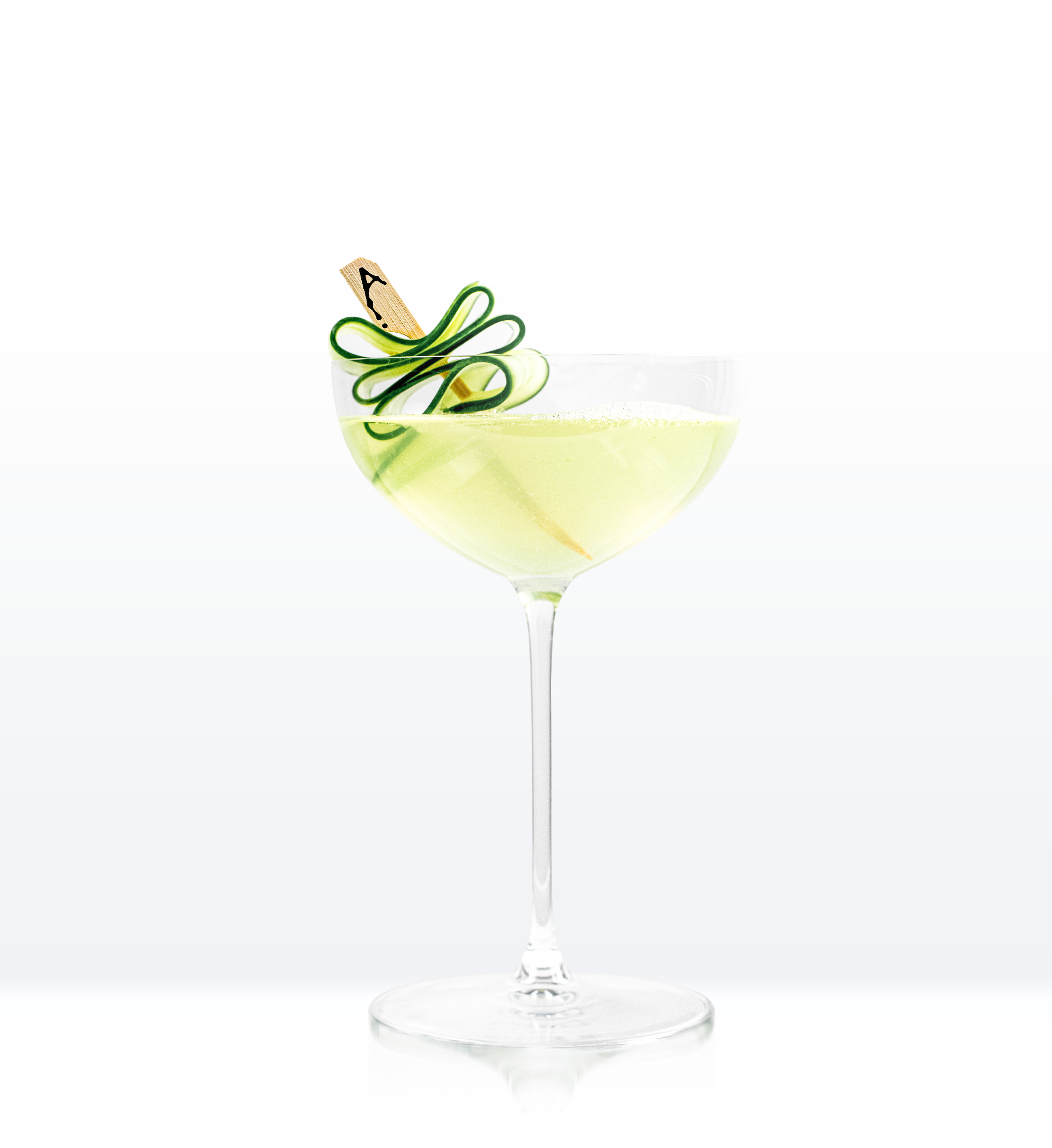 Light green cocktail in coupe glass with cucumber ribbon on a skewer with a letter A
