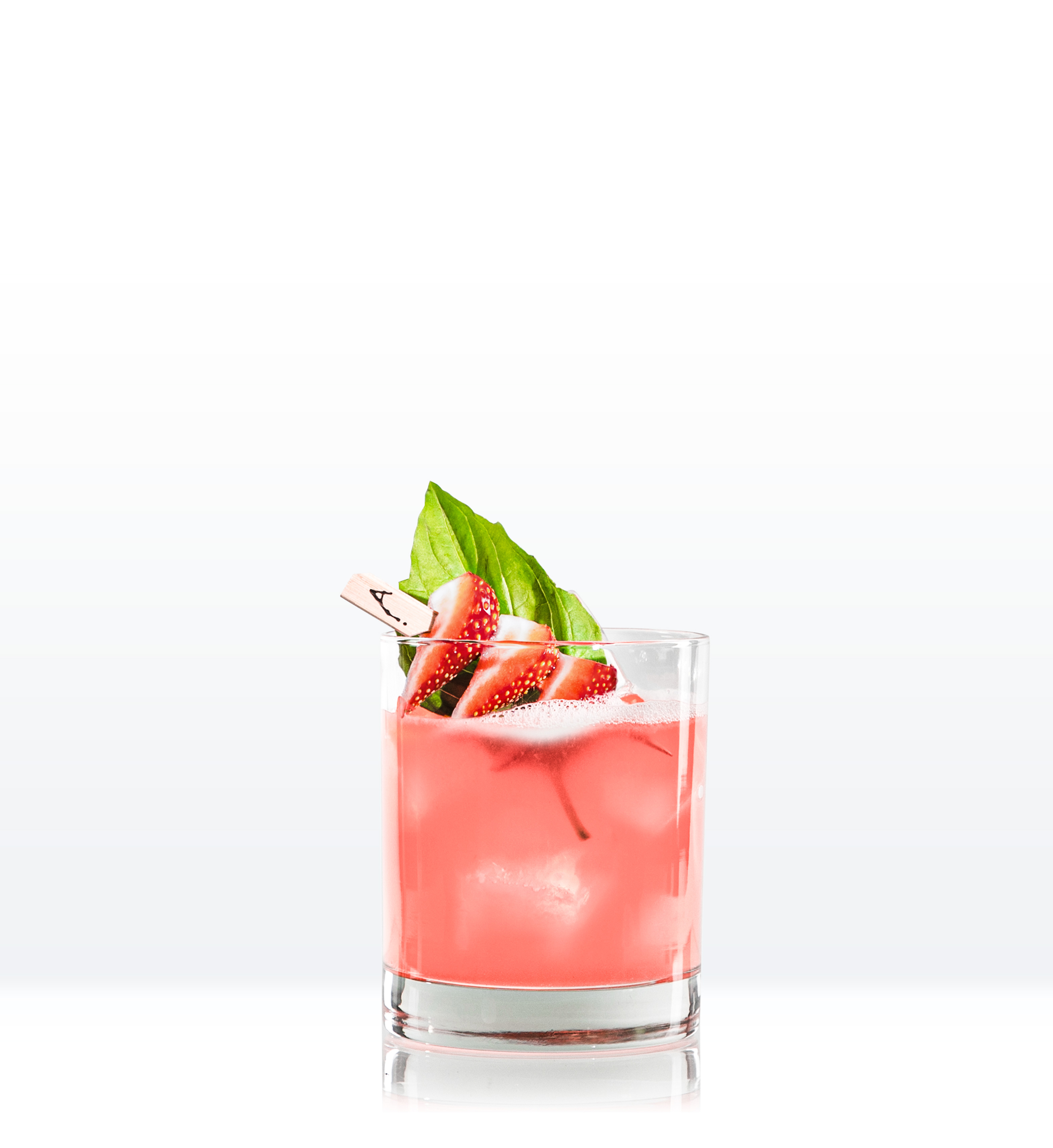 Red cocktail in lowball glass garnished with strawberries on skewer and basil leaf