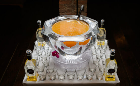 Orange event punch in punch bowl made of ice with glasses and liquor bottles around
