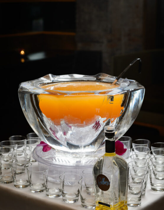 Orange event punch in punch bowl made of ice with glasses and liquor bottle around