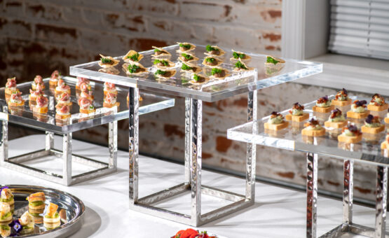 Event food station with multiple hors d'oeuvres on acrylic platters on stainless steel elevations