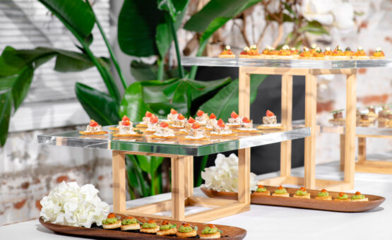 Wooden elevations and acrylic trays with multiple hors d'oeuvres and green leaves in background