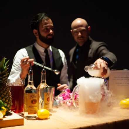 Two mixologists behind the bar making dry ice cocktail in a pitcher