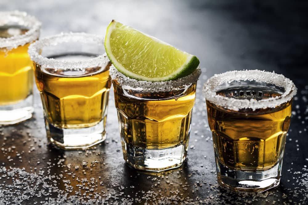 Several glasses of tequila with salted rims and a lime wedge